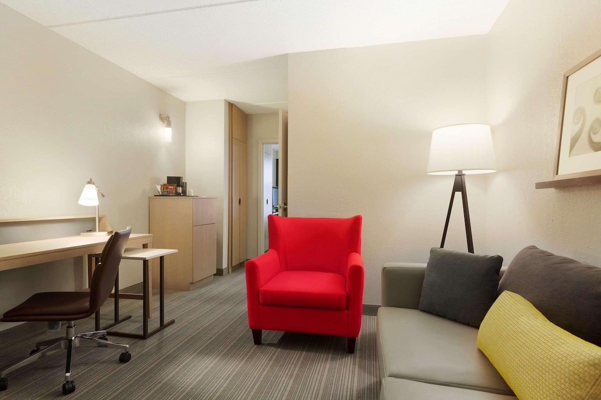 Hotellihuone, jossa on työpöytä, punainen nojatuoli, sohva ja lattiavalaisin.
