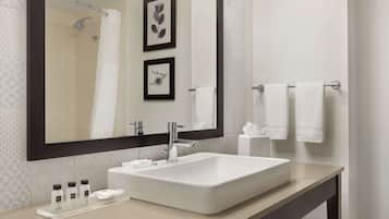 Un baño moderno con un espejo grande, un lavamanos blanco y dos cuadros enmarcados en la pared.