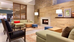 A modern living room with a fireplace, wooden wall paneling, and a dining area in the background.