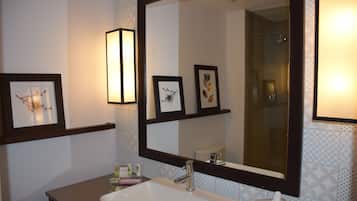 A bathroom with a large mirror, framed artwork, and a sink with toiletries.