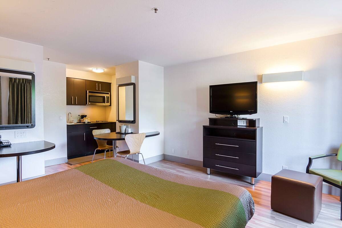 A hotel room with a bed, a desk, a chair, a television, a microwave, and a small kitchenette.