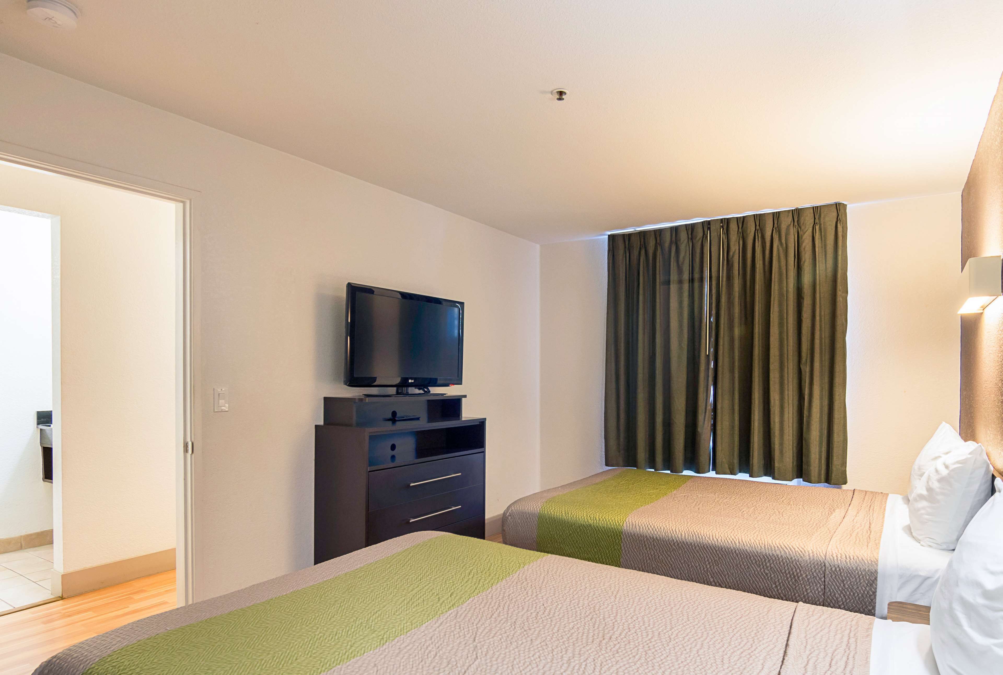A hotel room with two beds, a TV on a dresser, and a window with curtains.