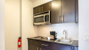 A compact kitchenette with a microwave, stove, sink, and cabinets.
