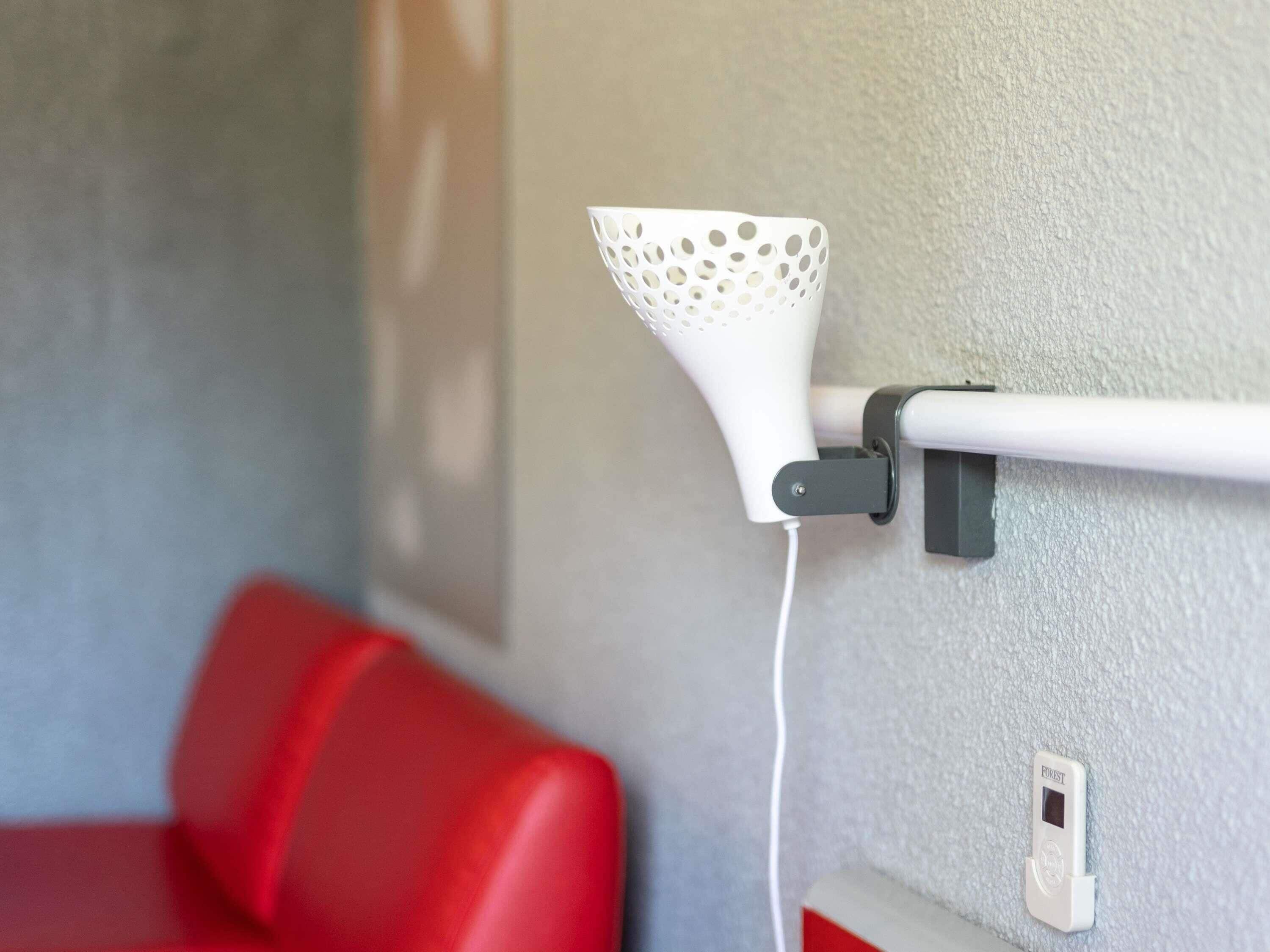 A white wall-mounted badminton shuttlecock holder attached to a white wall, with a red chair visible in the background.