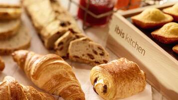 A variety of baked goods including croissants and bread, arranged on a wooden surface with a label reading "Ibis Kitchen".