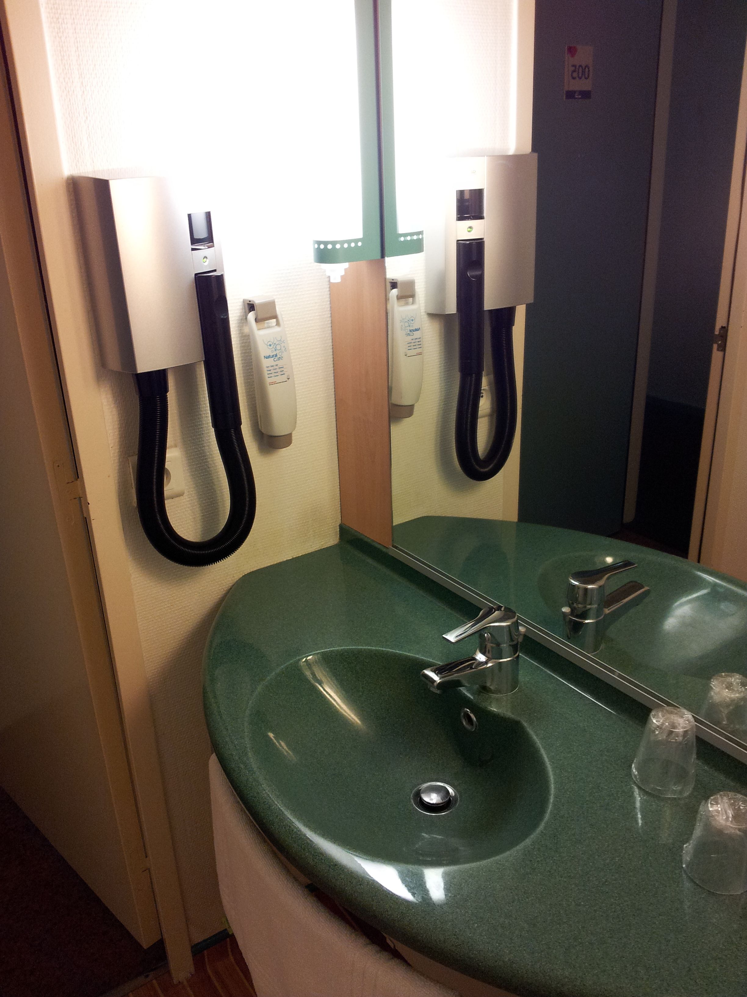 Un baño con un lavabo verde, un espejo, un teléfono y un secador de manos.