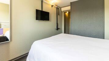 Habitación de hotel con una cama, un televisor de pantalla plana montado en la pared y una lámpara.