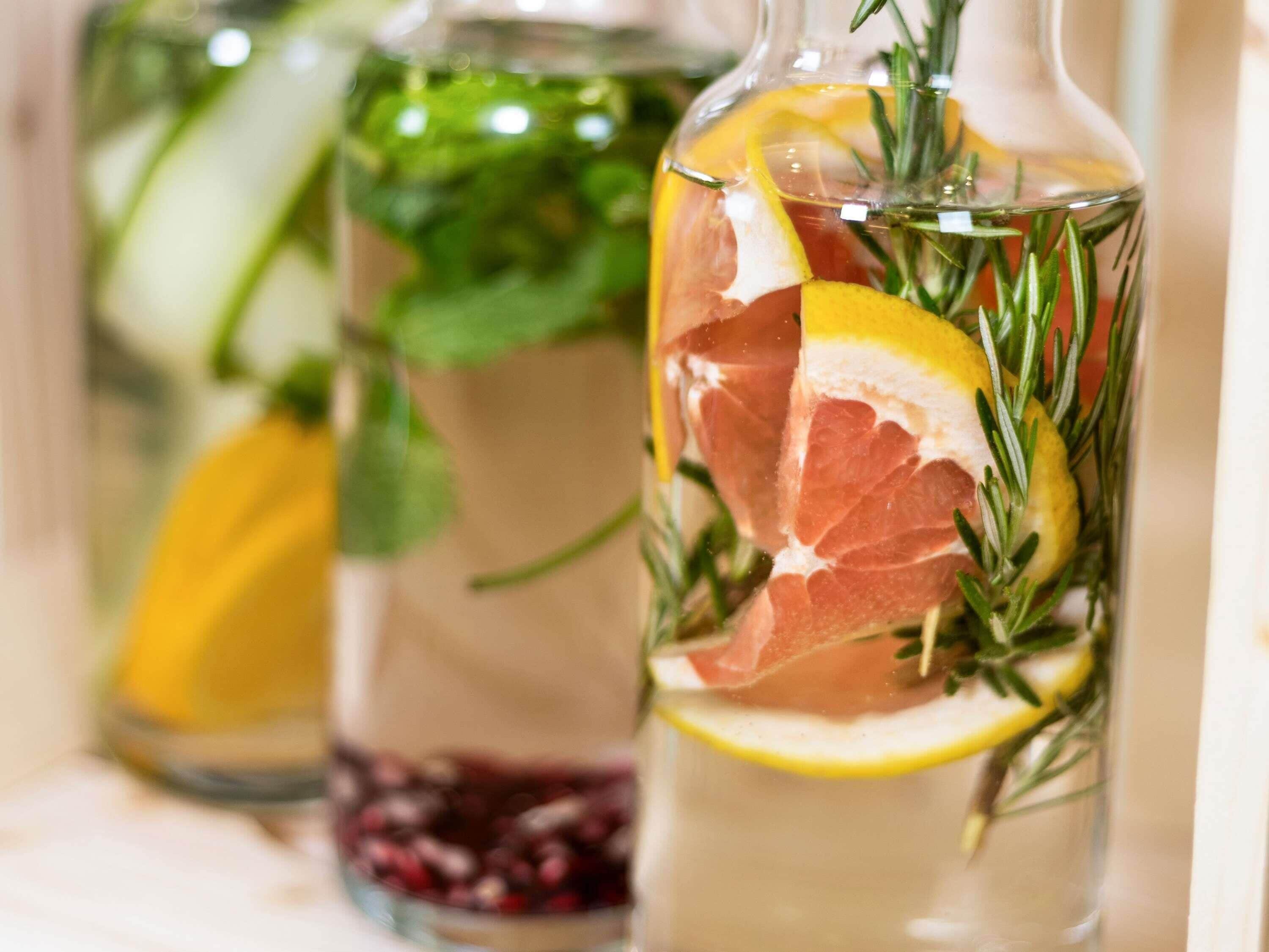 Three glass bottles with herbal infusions, containing slices of citrus and herbs.
