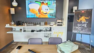 A modern office space with a large TV displaying a cartoon character, a coffee station, and a motivational poster.