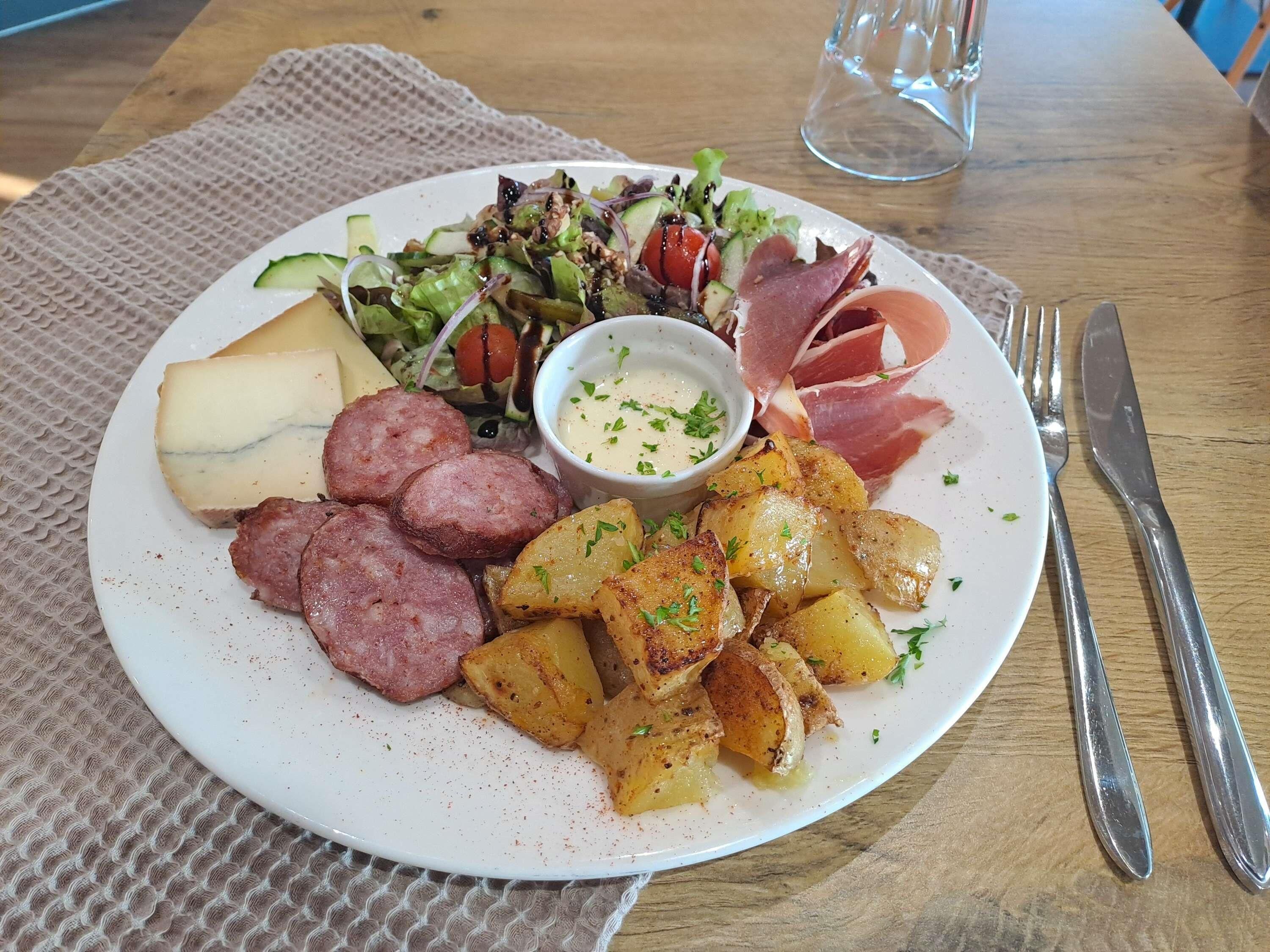 Un plato de comida con salchichas, patatas, queso y una ensalada con salsa para mojar.