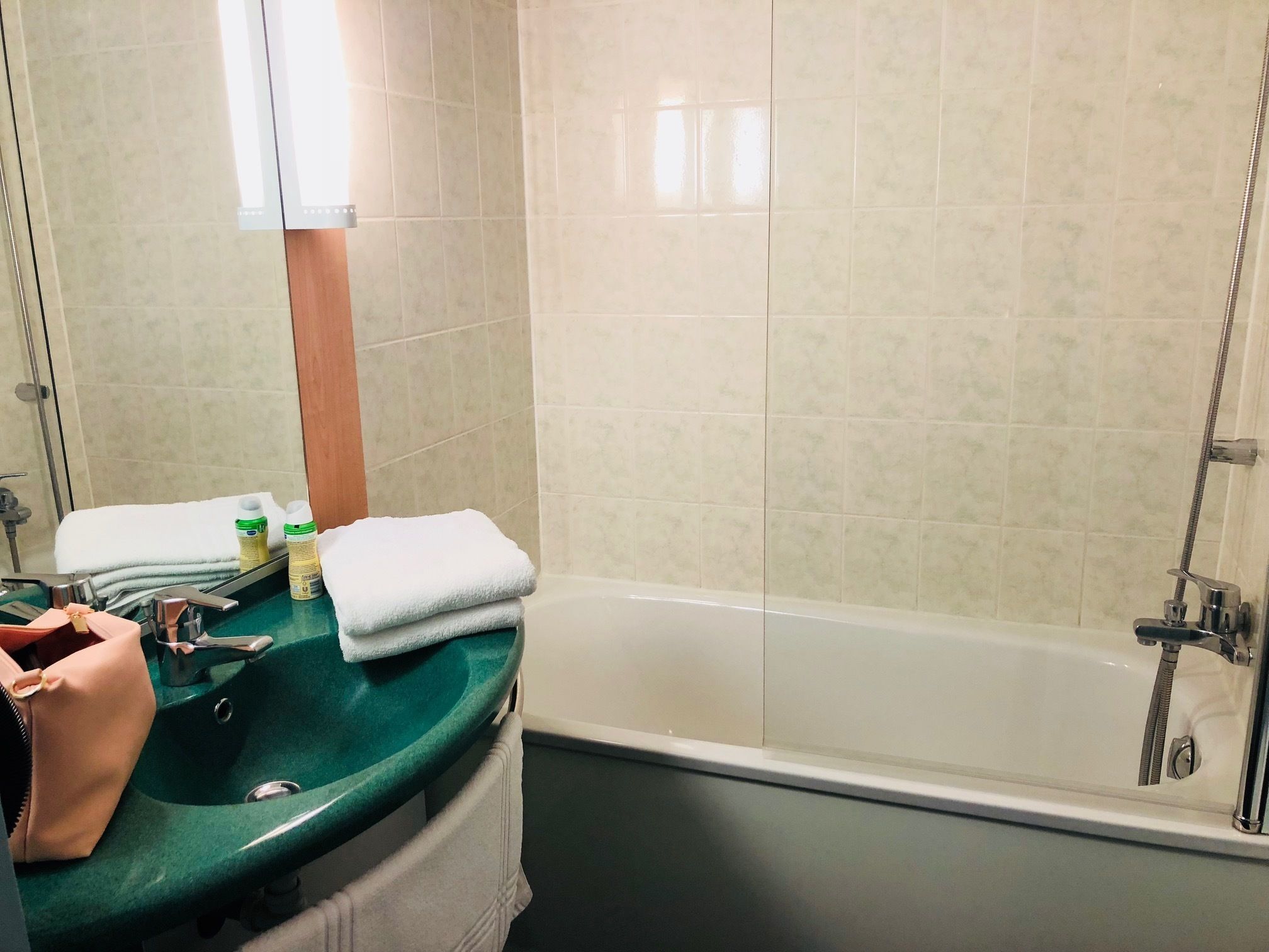 A bathroom with a green sink, white bathtub, and beige tiled walls.