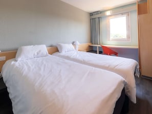 A hotel room with two beds, a desk, a chair, and a window with curtains.