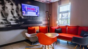 Un'area lounge moderna con un divano, poltrone, un tavolino e un televisore che mostra un notiziario.