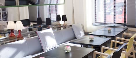 A modern hotel lobby with a sofa, tables, chairs, and a large mirror.