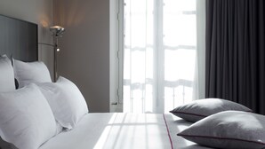 A hotel room with a large bed, a bedside lamp, and a view of the outdoors through a window. - Hotel Saint Dominique (Paris)