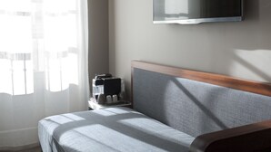 A neatly made bed with a grey headboard, a bedside table with a coffee maker, and a television mounted on the wall. - Hotel Saint Dominique (Paris)