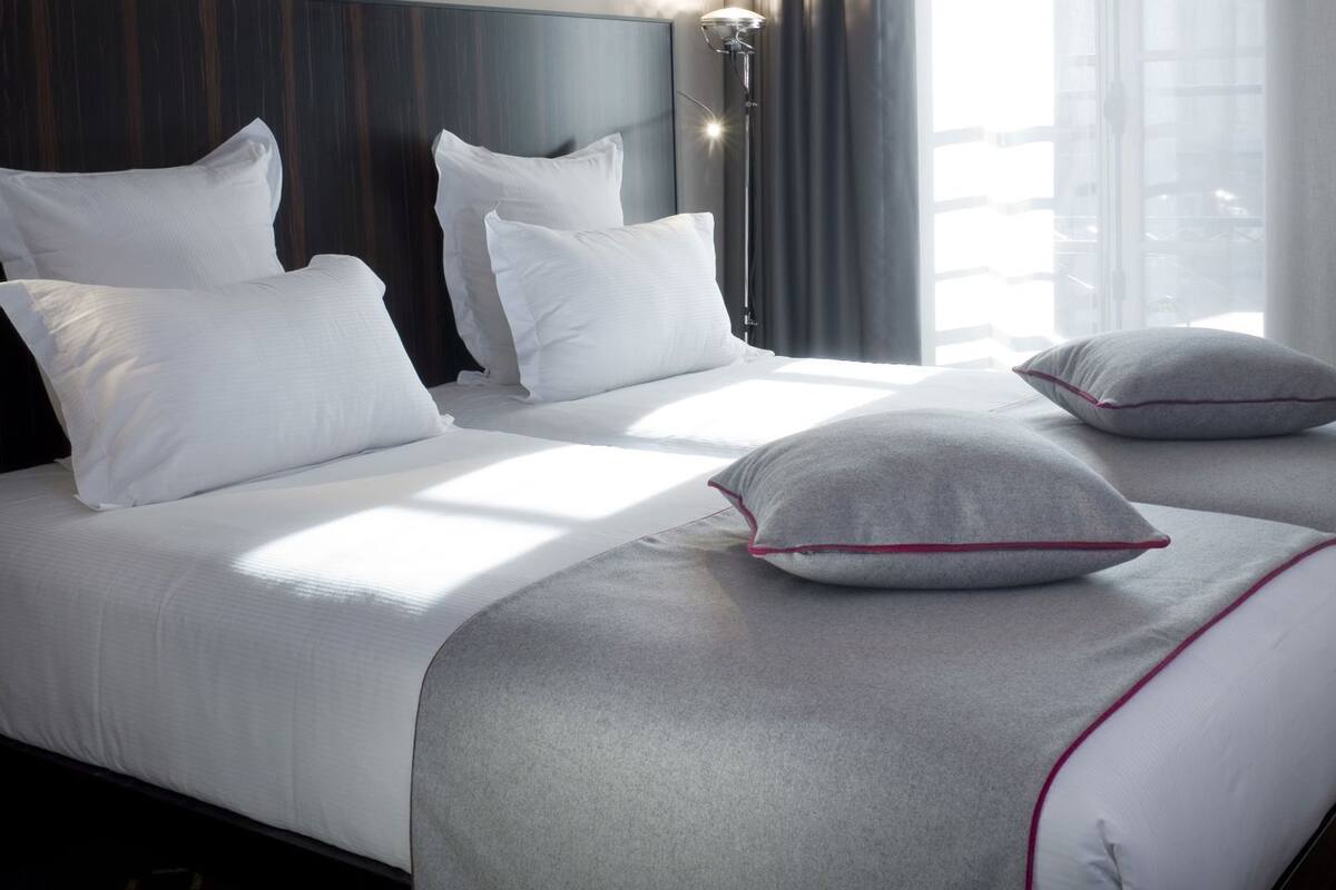 A hotel room with a large bed, a headboard, a floor lamp, and a window with curtains.