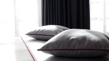A bed with two pillows and a red accent on the bedspread, positioned next to a window with black curtains.