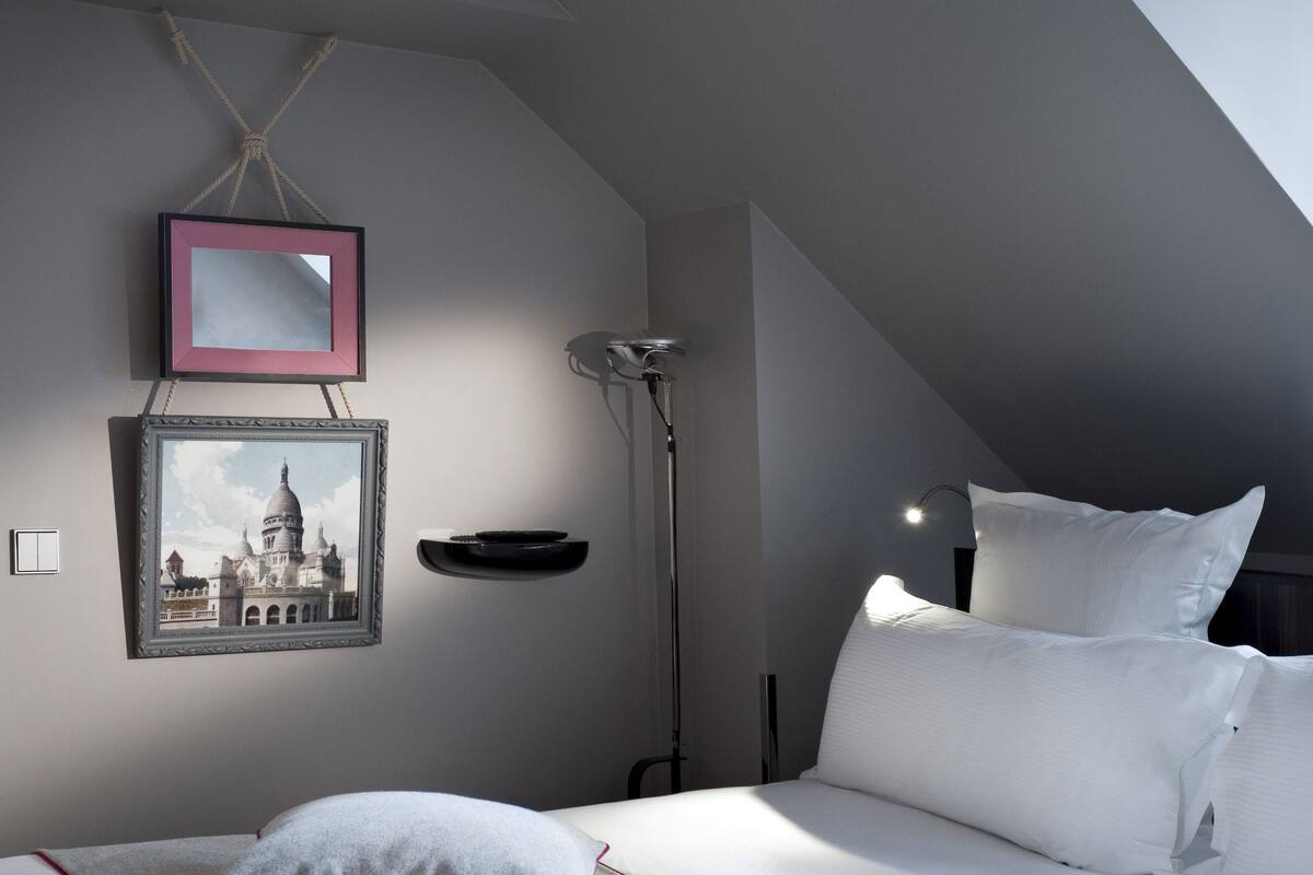 A bedroom with a bed, pillows, a framed picture, a floor lamp, and a ceiling light.