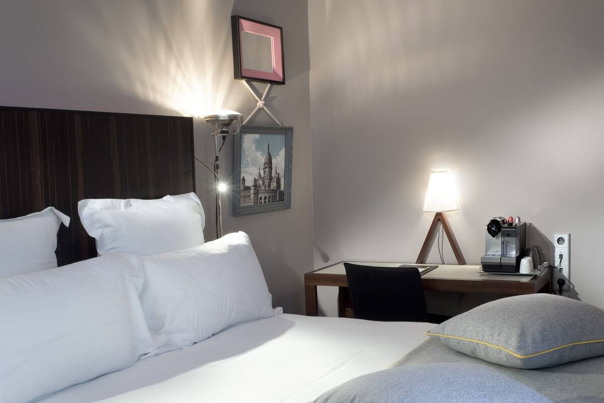 A hotel room with a large bed, a desk with a lamp, and a coffee machine.