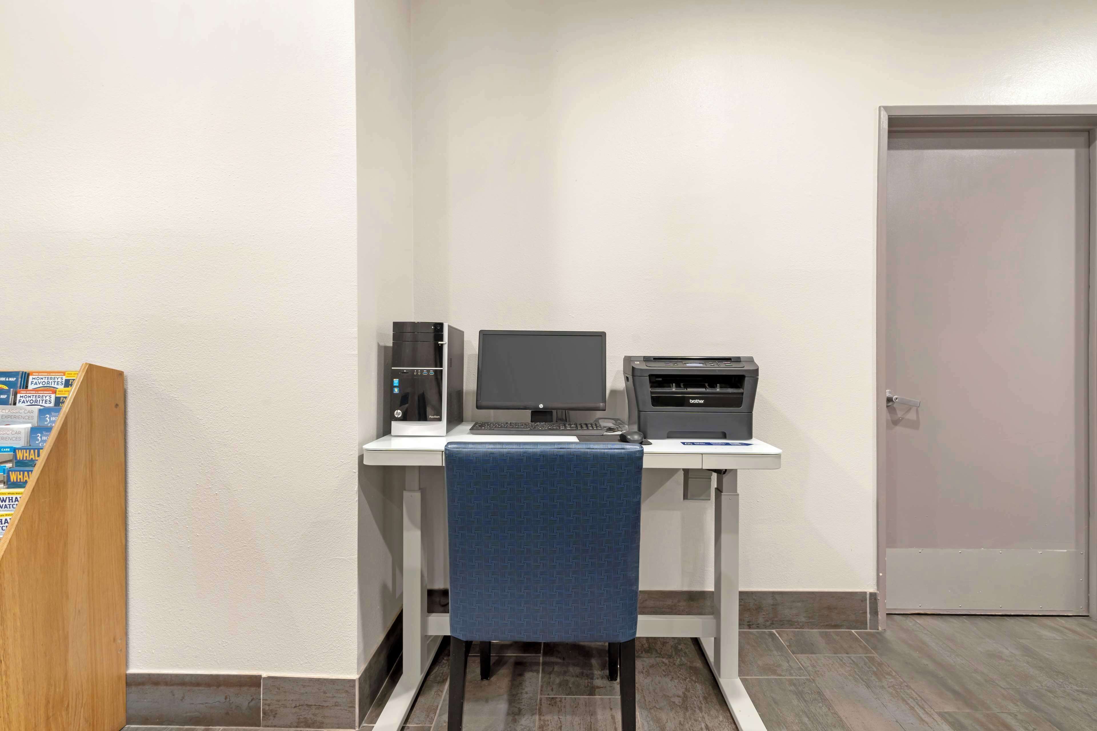 A computer desk with a monitor, keyboard, and printer. There is a blue chair in front of the desk. A door is visible to the right.