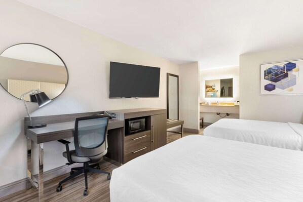A hotel room with a desk, a TV, a bed, and a bathroom with a mirror and sink.