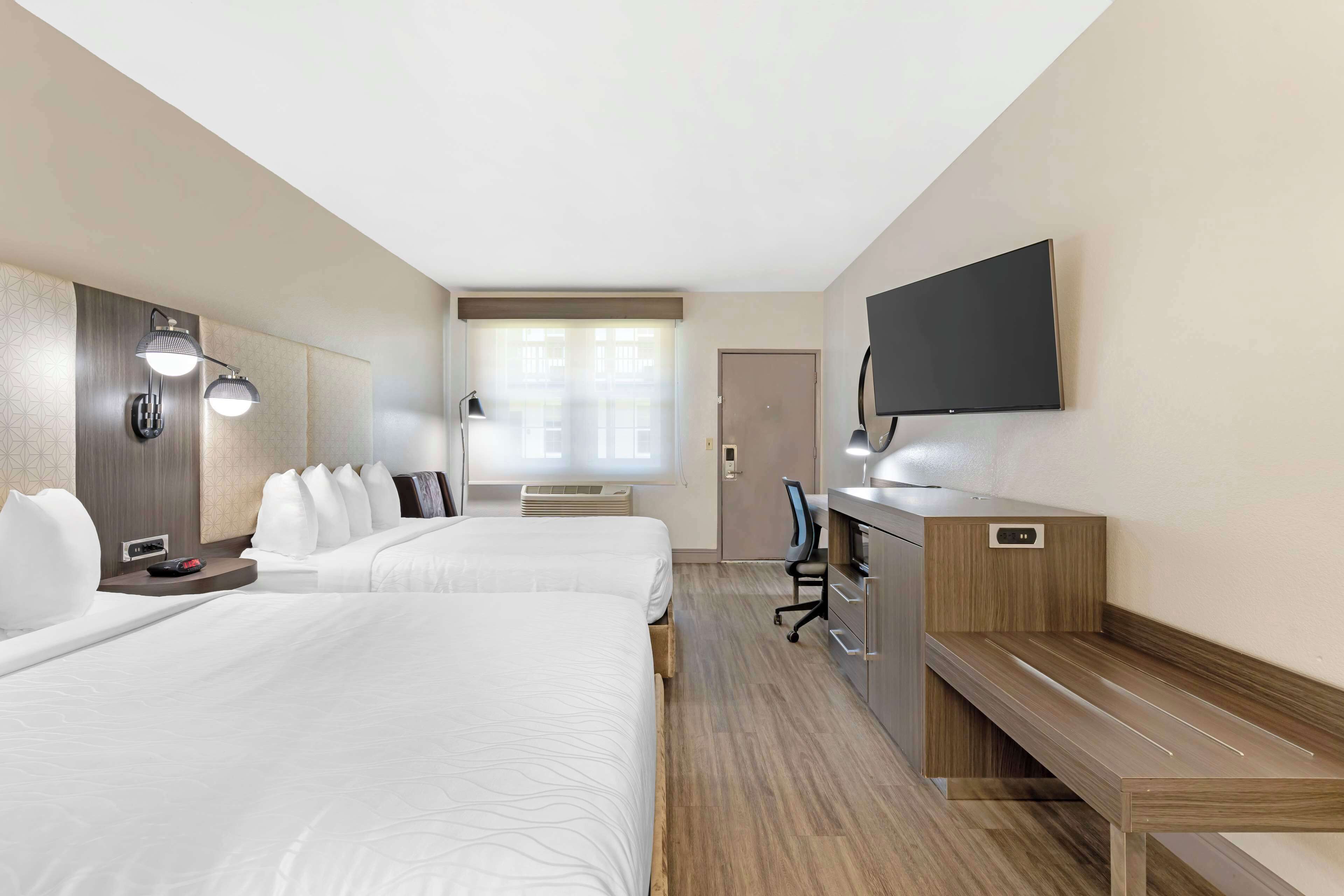 Une chambre d’hôtel avec deux lits, un bureau, un téléviseur à écran plat et une fenêtre avec des stores.
