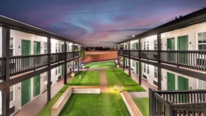 A hotel courtyard with green lawns, a tennis court, and multiple rooms with green doors. - Best Western Marina State Beach (Marina)