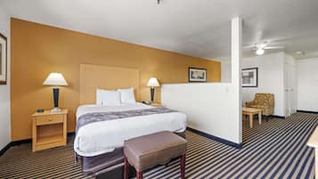 Habitación de hotel con cama, dos mesitas de noche con lámparas, un banco, una silla y una puerta que da a otra habitación.
