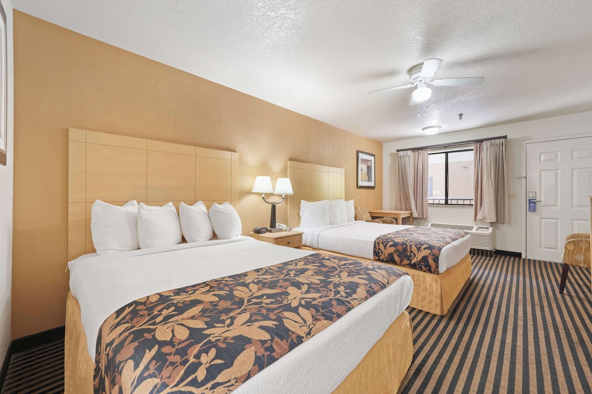 A hotel room with two beds, a ceiling fan, a window with curtains, and a door.