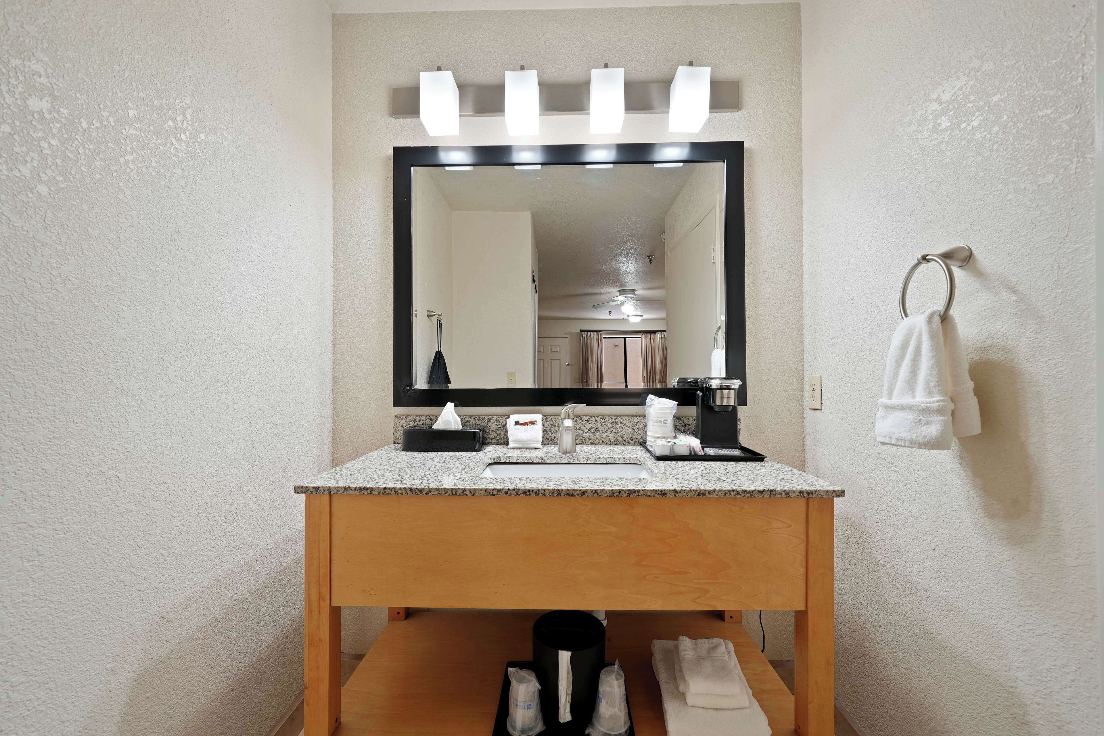 A bathroom with a wooden vanity, a large mirror with lights, a towel rack, and a sink.