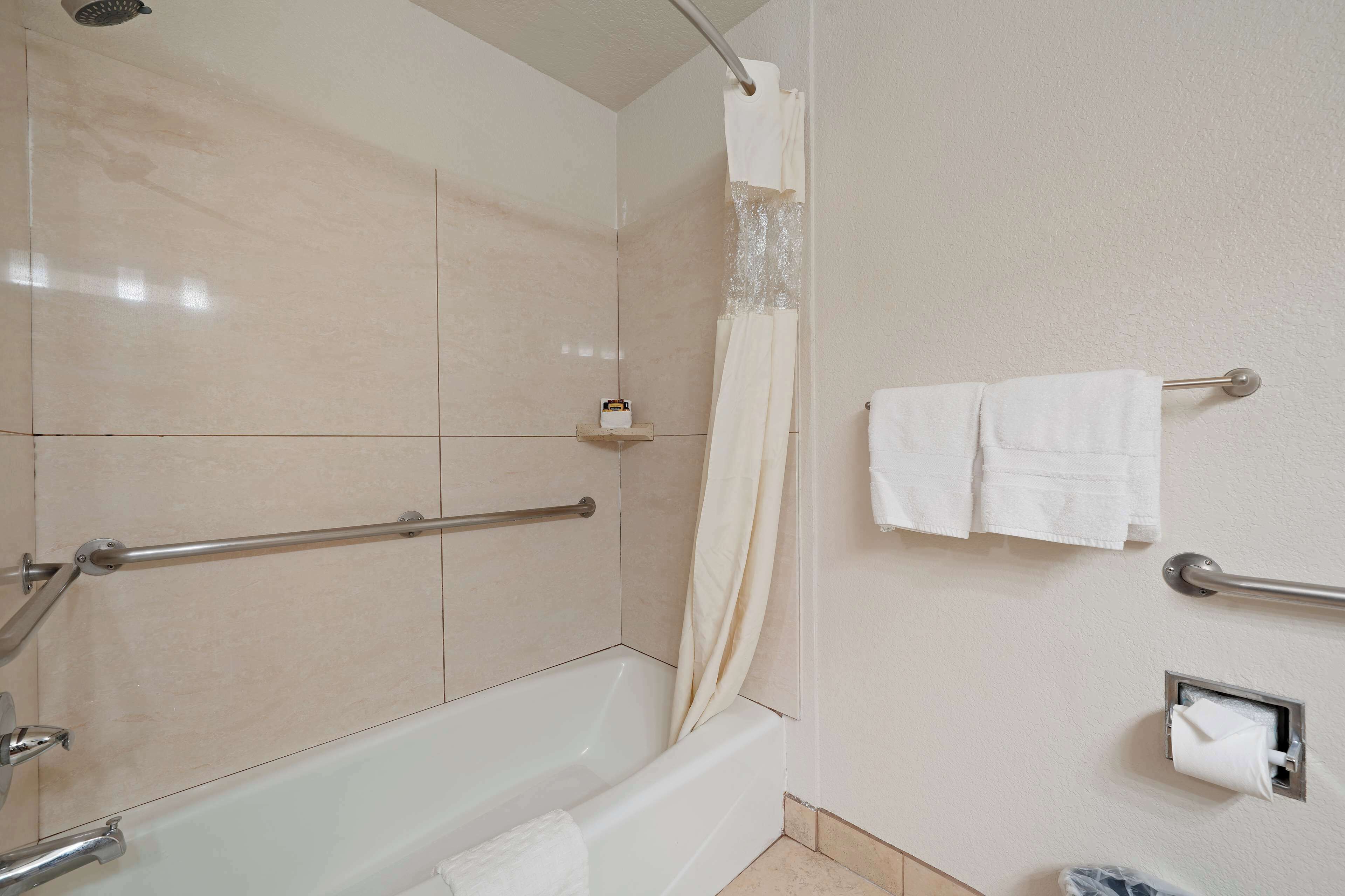 A bathroom with a bathtub, a shower curtain, a towel rack with towels, and a toilet paper holder.