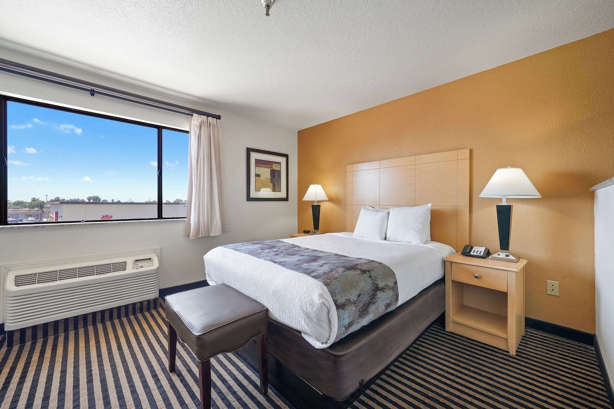 A hotel room with a large bed, bedside lamps, a heater, a window with curtains, and a view of the city.