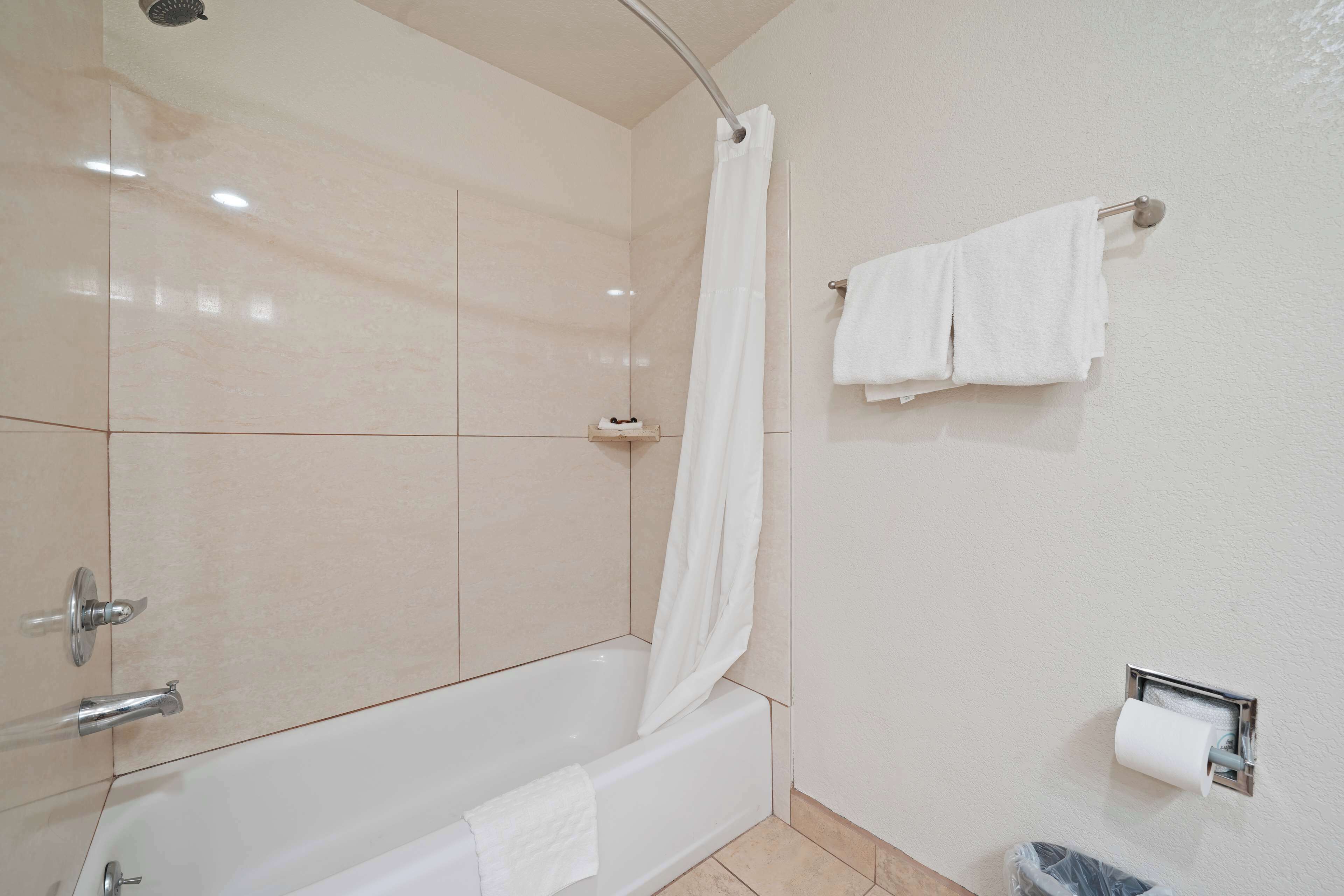 A modern bathroom with a bathtub, a shower curtain, a towel rack, and a toilet paper holder.