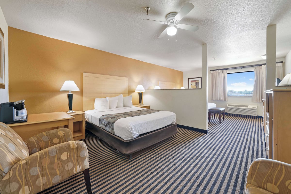 A hotel room with a large bed, two bedside tables with lamps, a desk, a chair, and a view of the outdoors.