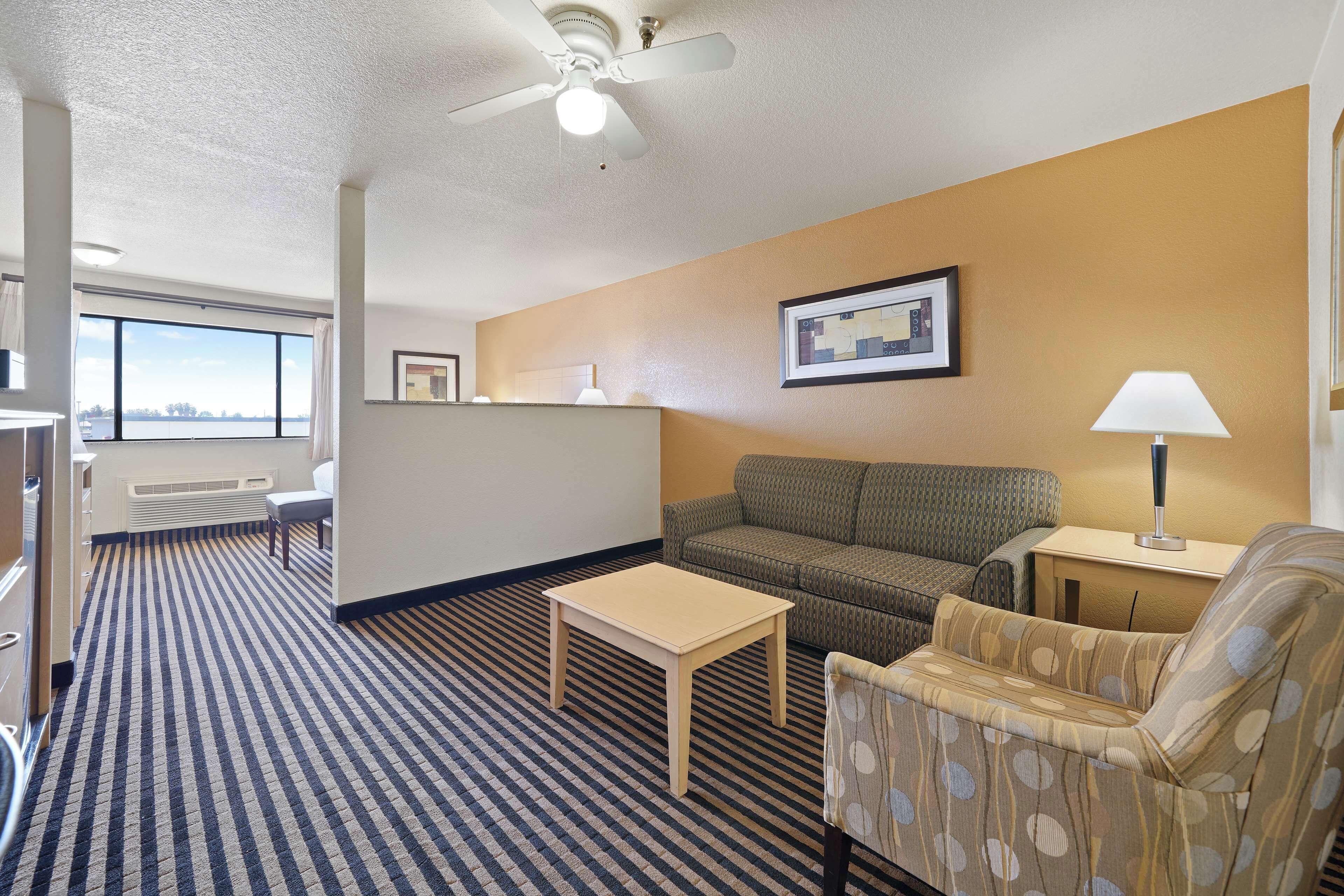 A hotel room with a large window, a sofa, a chair, a small table, and a lamp.