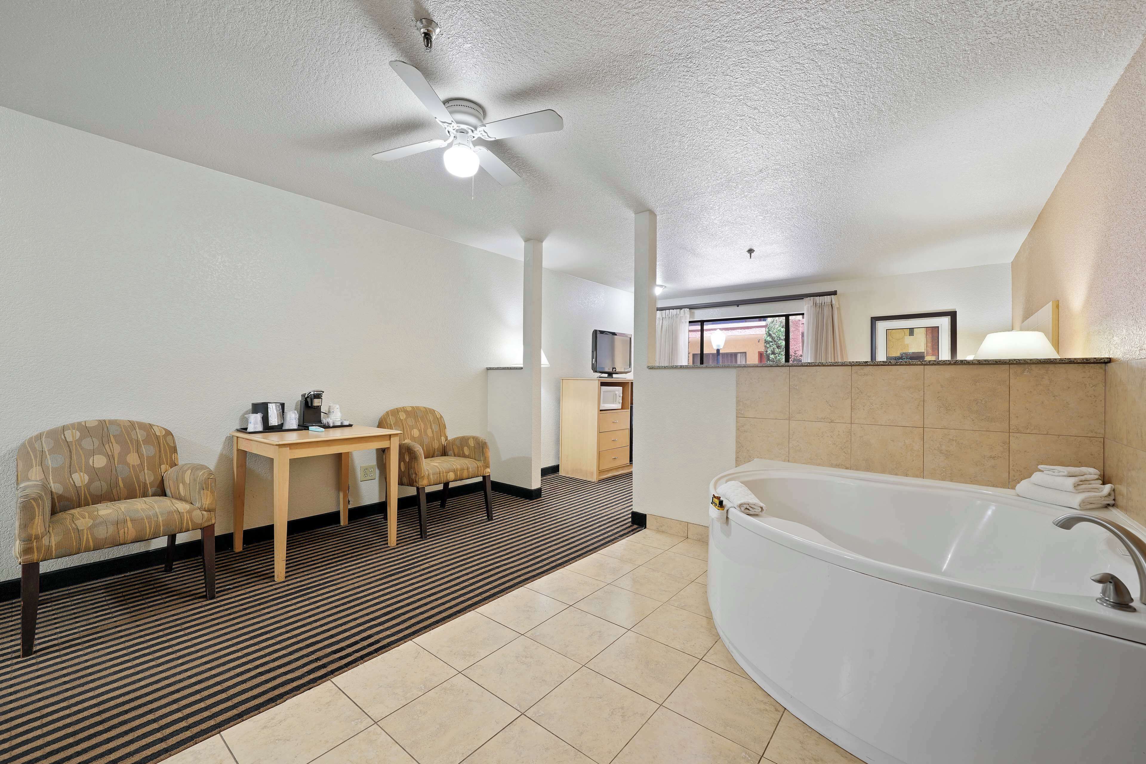 Un baño de hotel con una bañera, dos sillones, una mesita y un ventilador de techo.