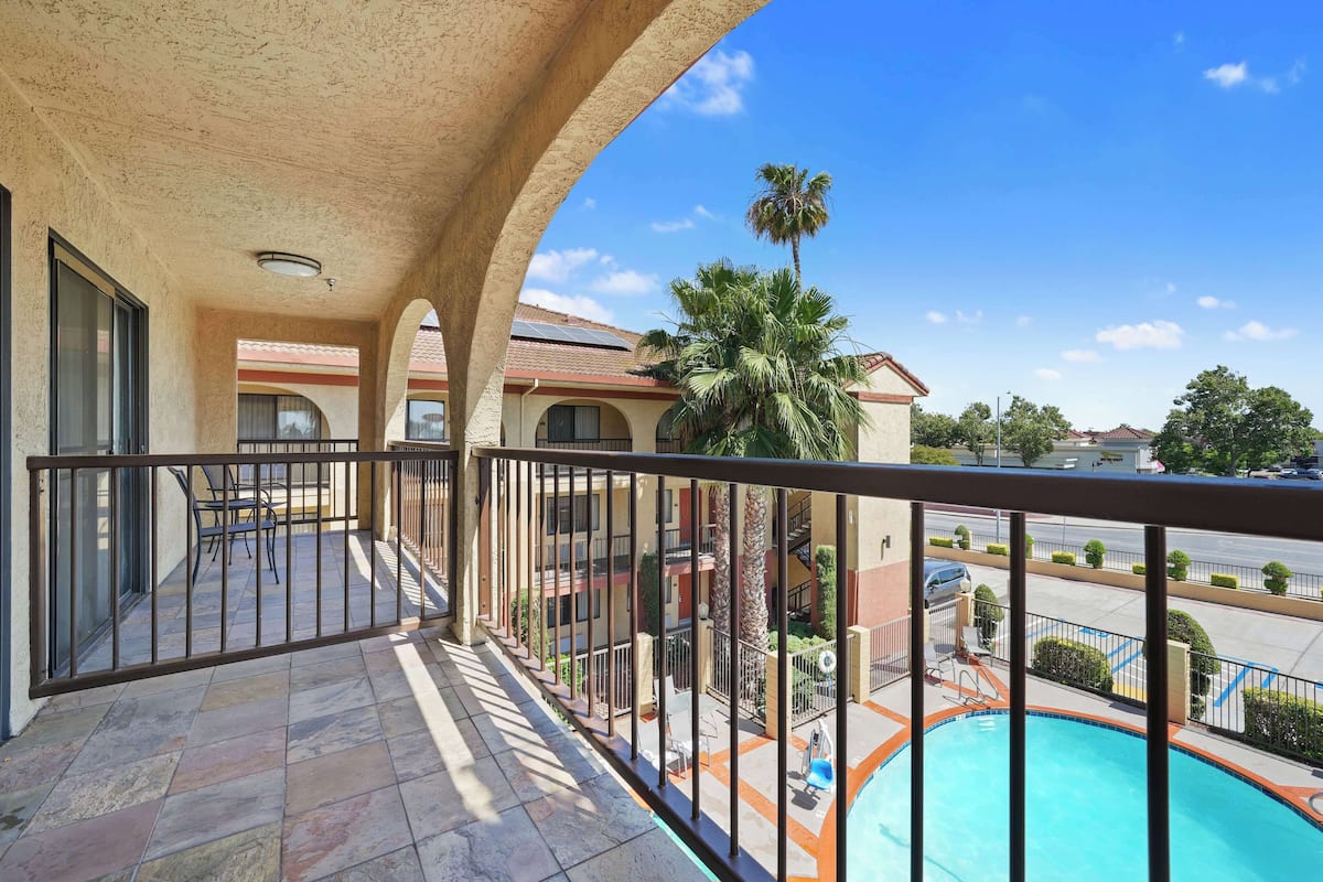 A balcony with a stone floor, a metal railing, and a view of a swimming pool and buildings in the background.