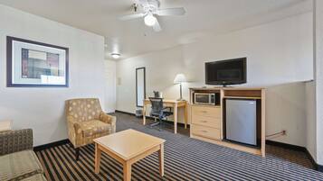 A hotel room with a bed, a desk, a chair, a television, a microwave, and a ceiling fan.