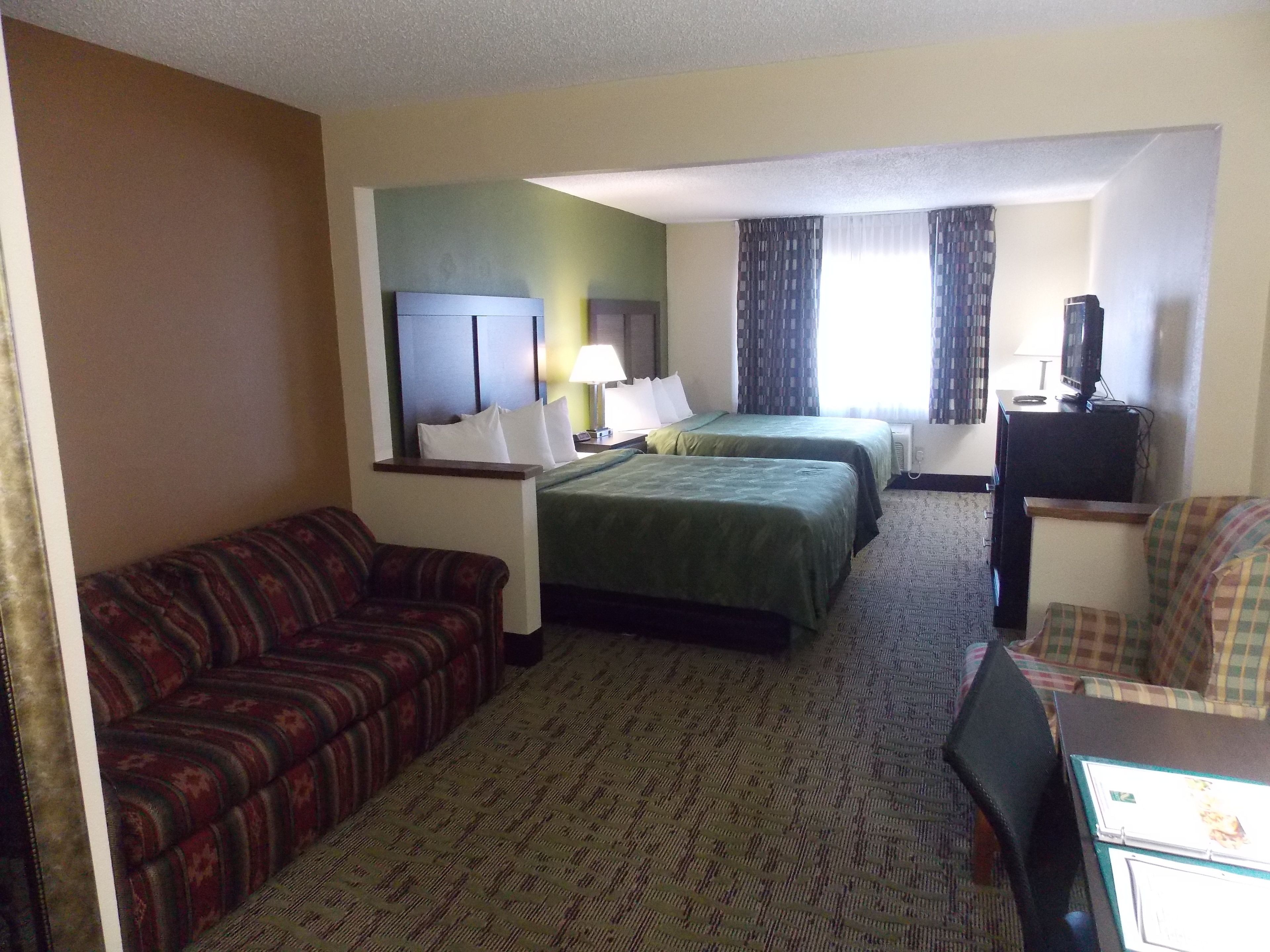 A hotel room with two beds, a sofa, a desk with a computer, and a television.