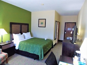 A hotel room with a bed, a desk, a chair, a television, and a door.