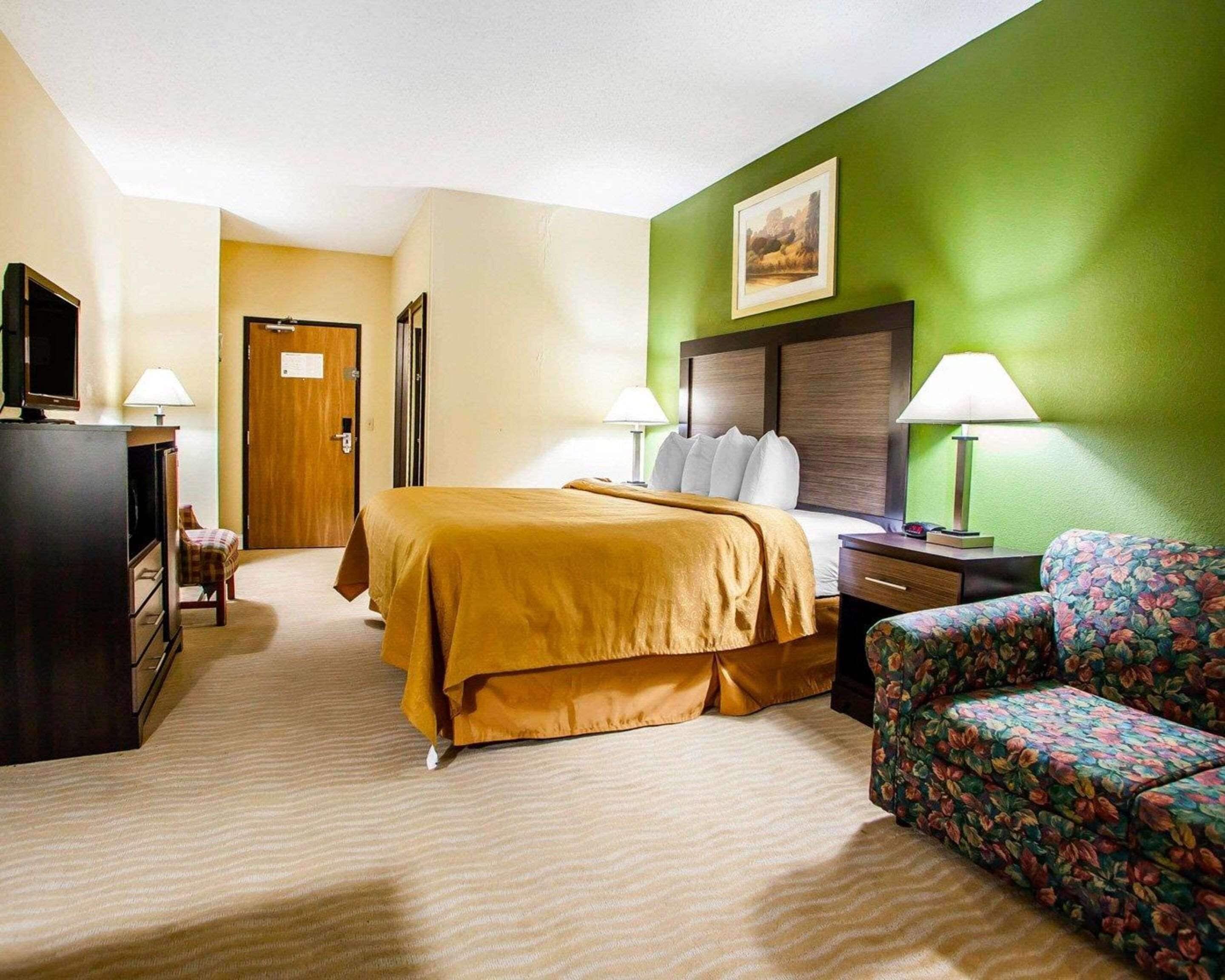 Una habitación de hotel con una cama, un televisor, un escritorio, una silla y una pared verde.