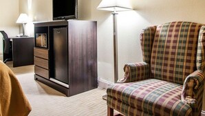 Ein Hotelzimmer mit Flachbildfernseher, Minibar, kariertem Ohrensessel und zwei Stehlampen.