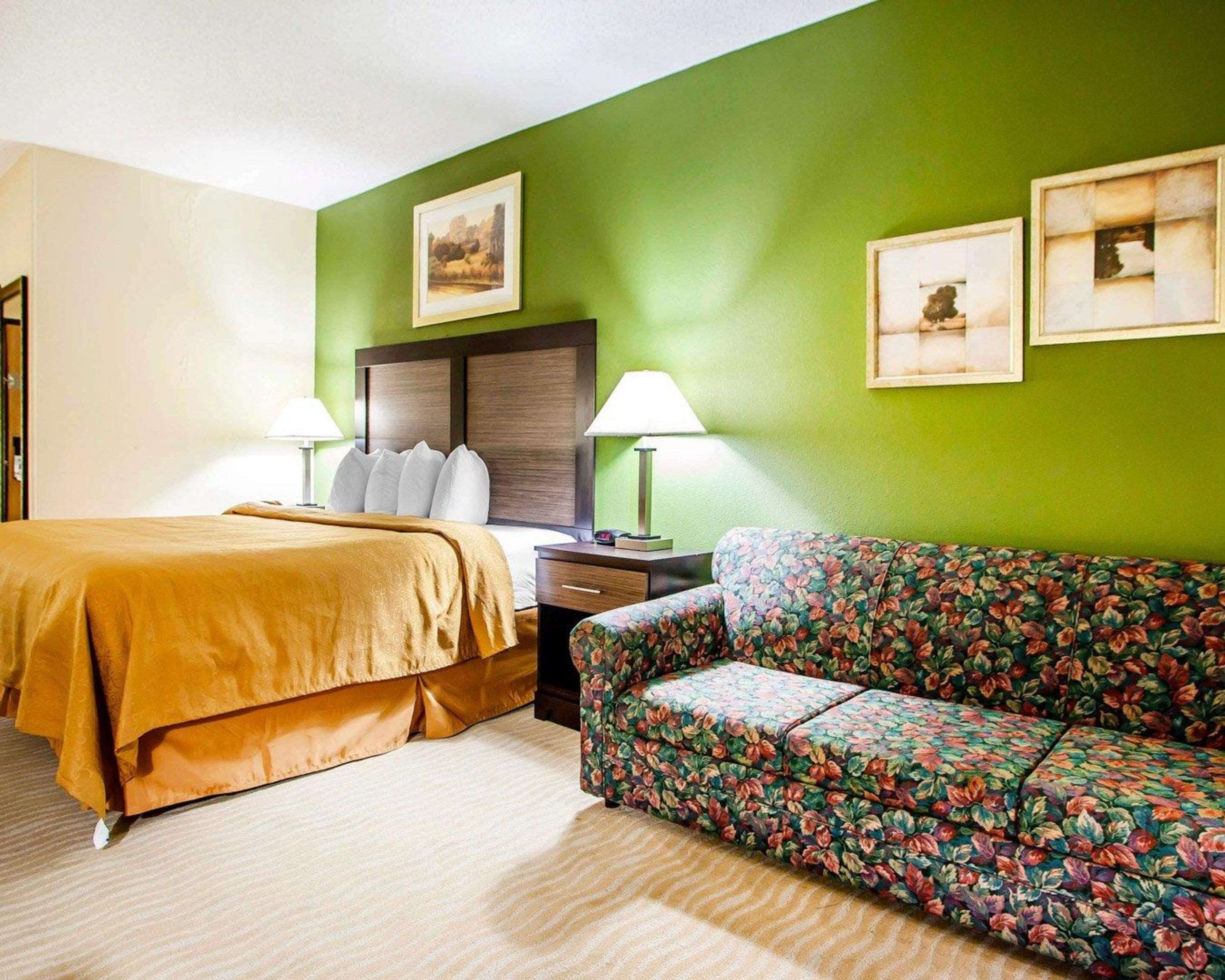 A hotel room with a bed, a floral sofa, two bedside lamps, and two framed pictures on the wall.