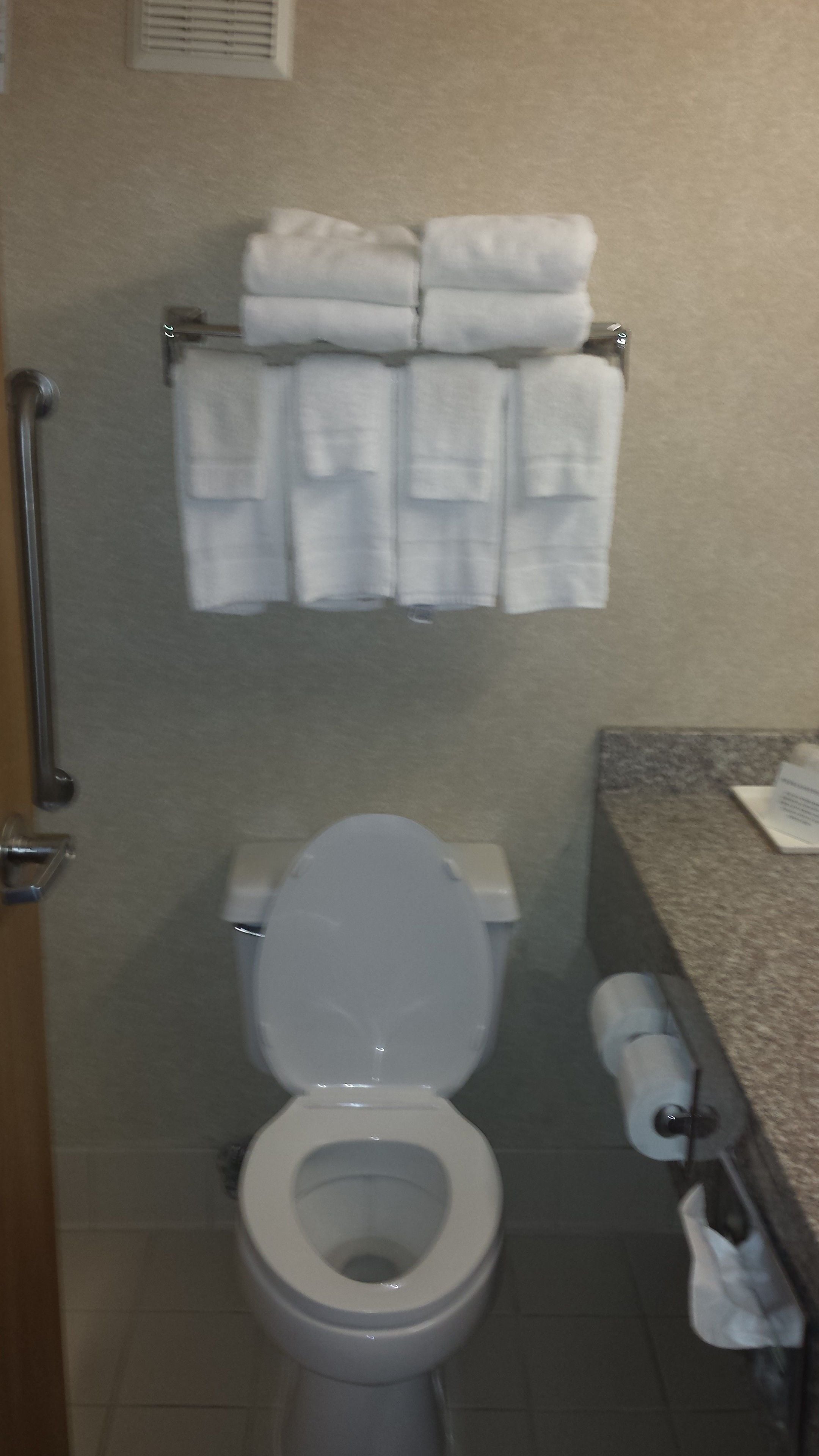Un baño con inodoro blanco, un perchero con toallas dobladas y un dispensador de toallas de papel.