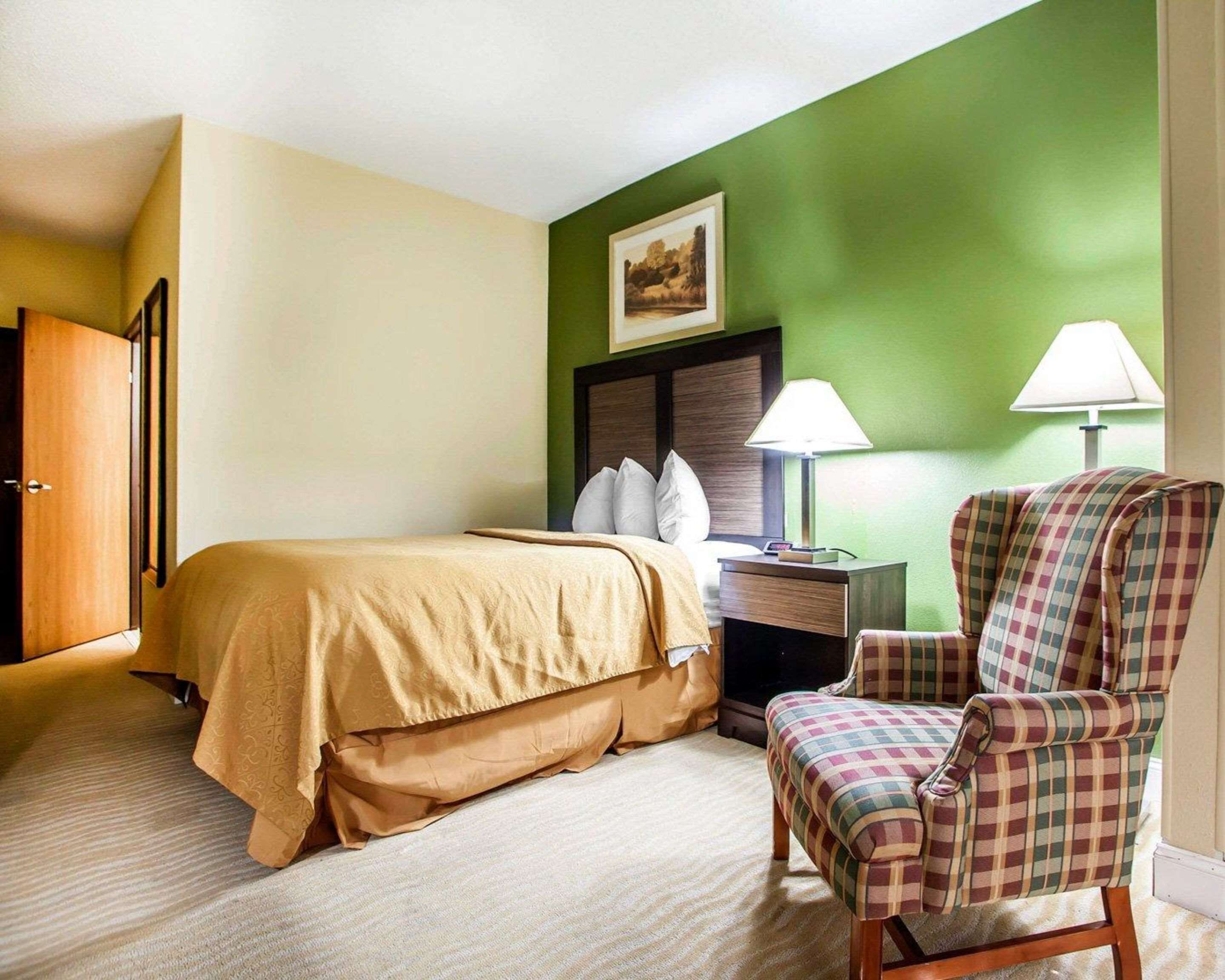 Una habitación de hotel con cama, silla, mesita de noche y lámpara.