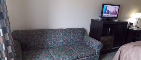 Une chambre d’hôtel avec un canapé à motifs floraux, un téléviseur posé sur un meuble et un lit recouvert d’une couvre-lit à motifs.