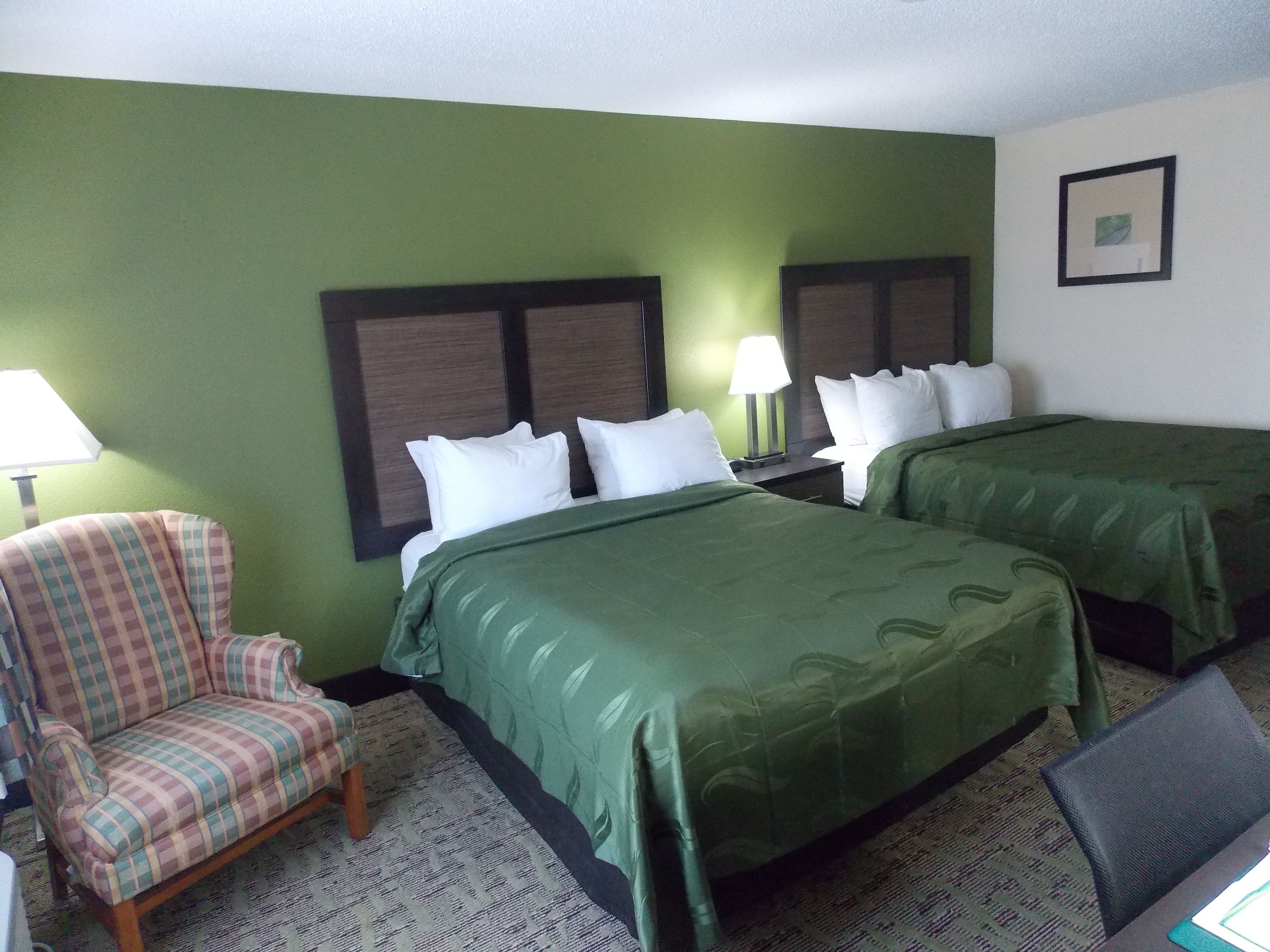 A hotel room with two beds, a chair, and a desk.