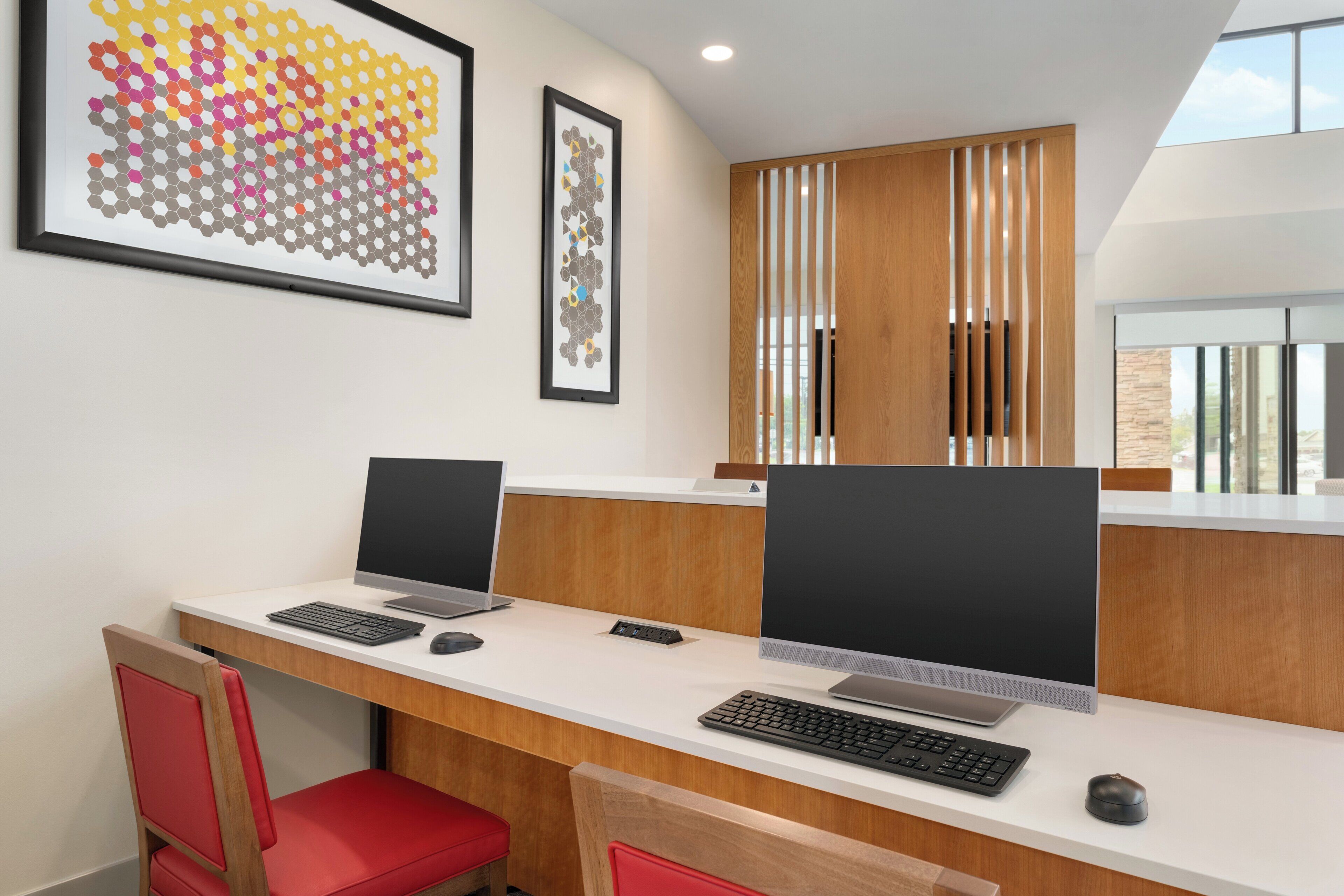 A modern office space with two desks, each with a computer and keyboard, and red chairs.