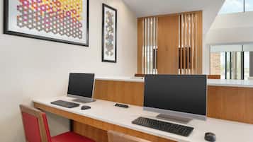 A modern office space with two desks, each with a computer and keyboard, and red chairs.